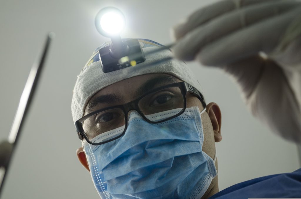 Surgeon looking down with instruments in hand and mask and glasses on face
